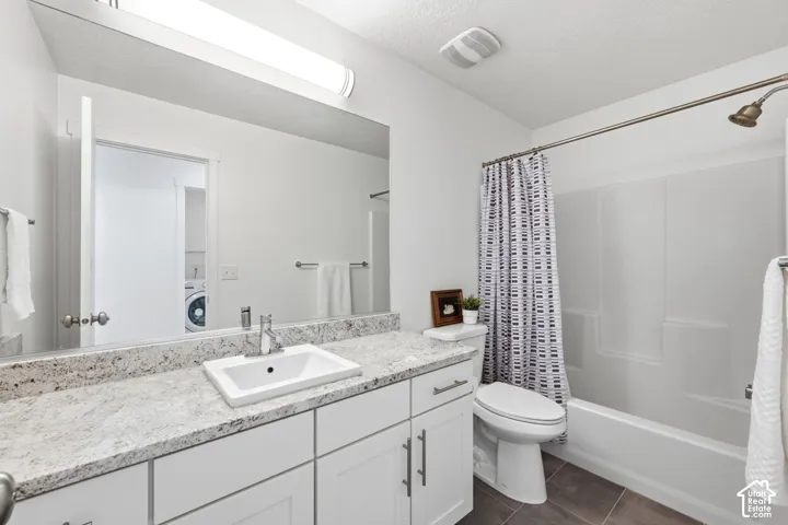 Bathroom featuring a vanity with a white rectangular sink, granite-patterned countertop, white cabinetry, a shower-tub combination, and dark tile flooring