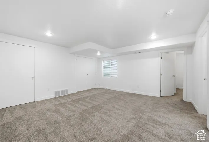 Spacious interior featuring neutral carpeting, recessed lighting, white walls, and bright window with horizontal blinds