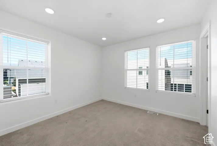 Bright, light-filled bedroom showcasing multiple windows with blinds, recessed ceiling lighting, neutral carpet flooring, and clean white walls