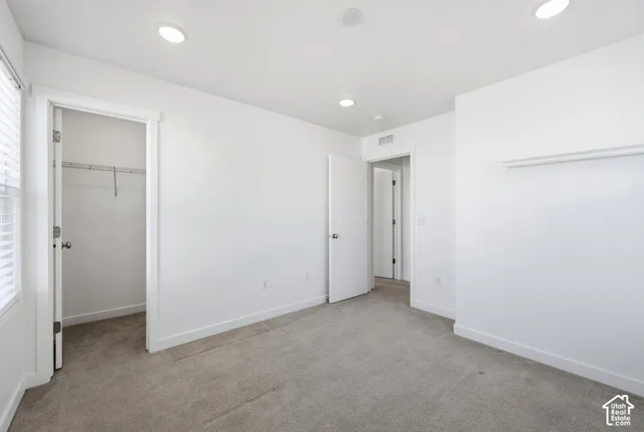 Recessed ceiling lighting, light gray carpeting, white walls, white trim, and a built-in closet system
