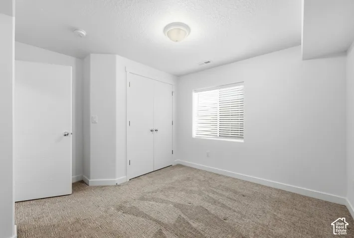 Neutral-toned carpet flooring, a window with blinds, and white bi-fold closet doors