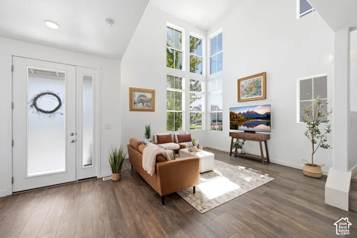 Soaring vaulted ceilings, expansive window wall with blinds, laminate flooring, recessed lighting, and a front entry door with frosted glass panels