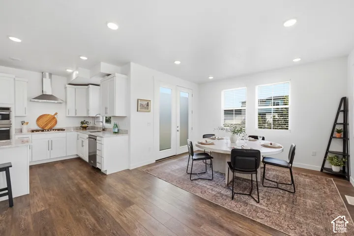 Open-concept kitchen with white cabinetry and stainless steel appliances, laminate flooring, recessed lighting, and a dining area with twin windows