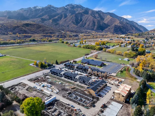 Mountain backdrop, adjacent green fields, established residential area, nearby commercial structures, new construction development