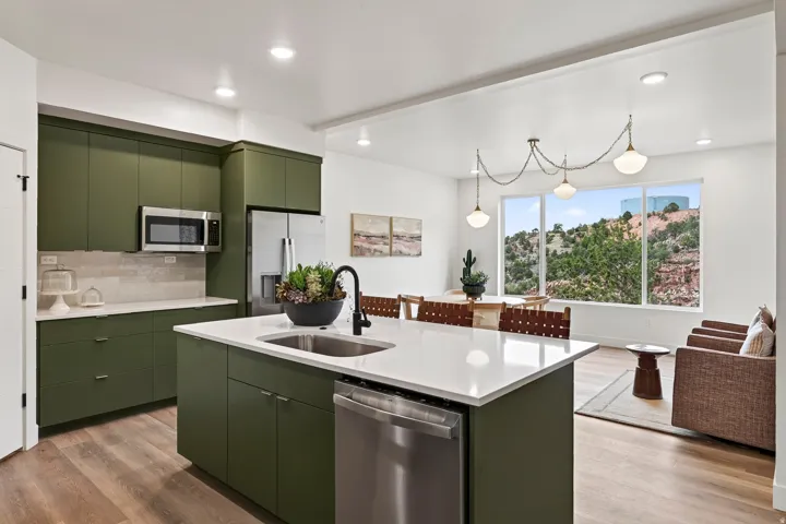 Open-concept living area featuring a kitchen island with sink, wood-finish flooring, recessed lighting, and a large window overlooking natural scenery