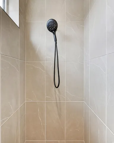 Shower enclosure featuring large format wall tiles with subtle veining and a matte black handheld shower fixture