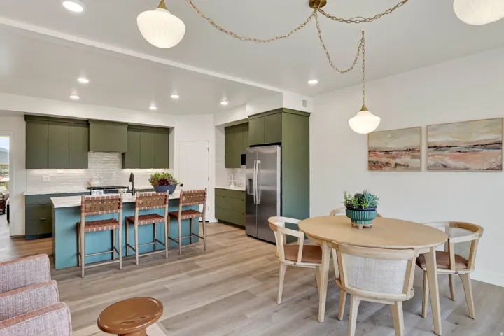 Modern kitchen featuring green cabinetry, a center island with seating, a stainless steel refrigerator, and wood-finish flooring