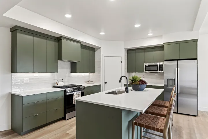 Modern kitchen featuring green flat-panel cabinetry, white countertops, stainless steel appliances, a tile backsplash, and a central island with an undermount sink