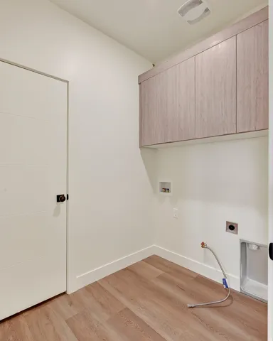 Wood-finish flooring, overhead cabinetry, and white paneled door with dark hardware