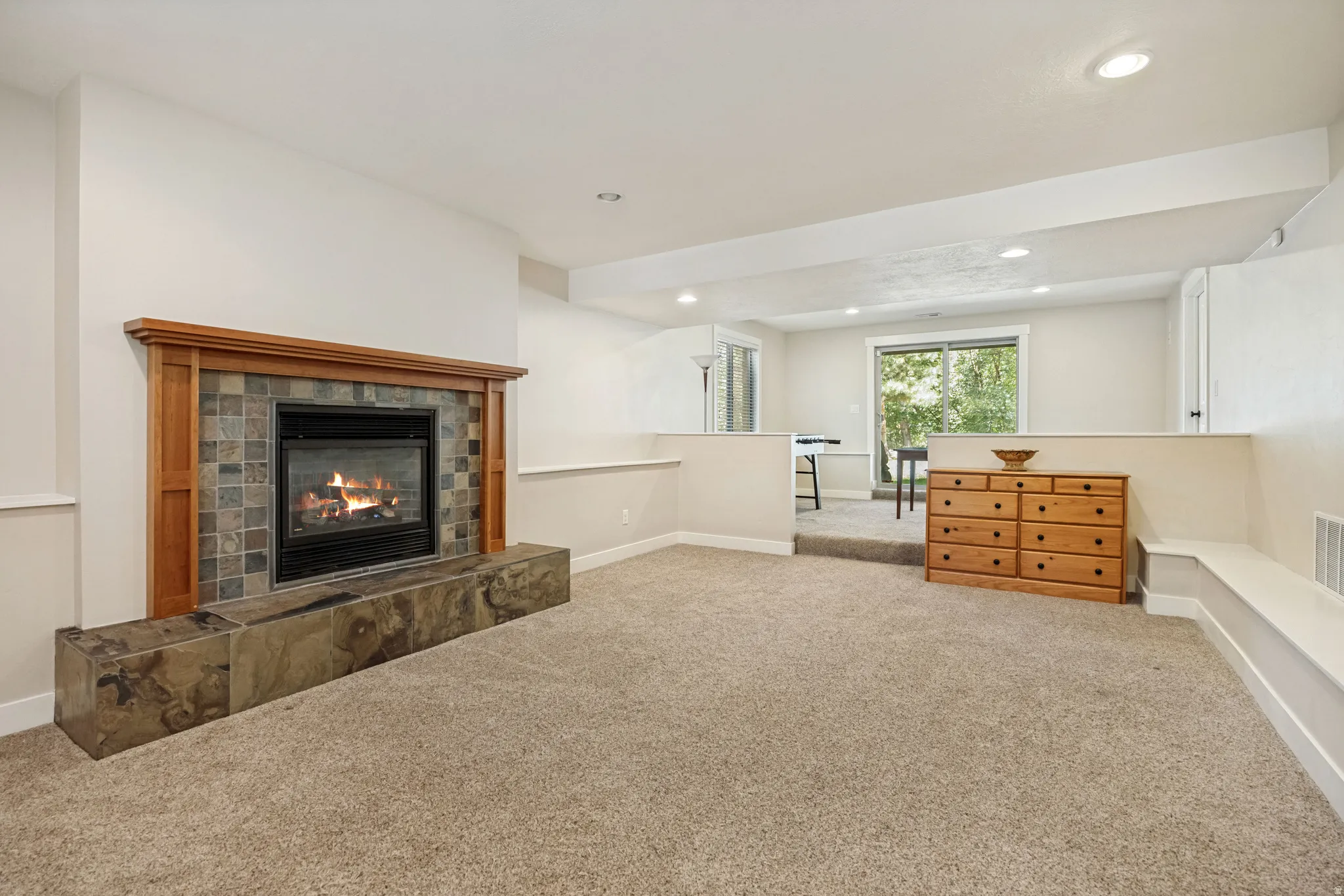 Carpeted living space featuring a fireplace with a wood mantle and stone tile surround, recessed lighting, and a raised section with sliding glass doors