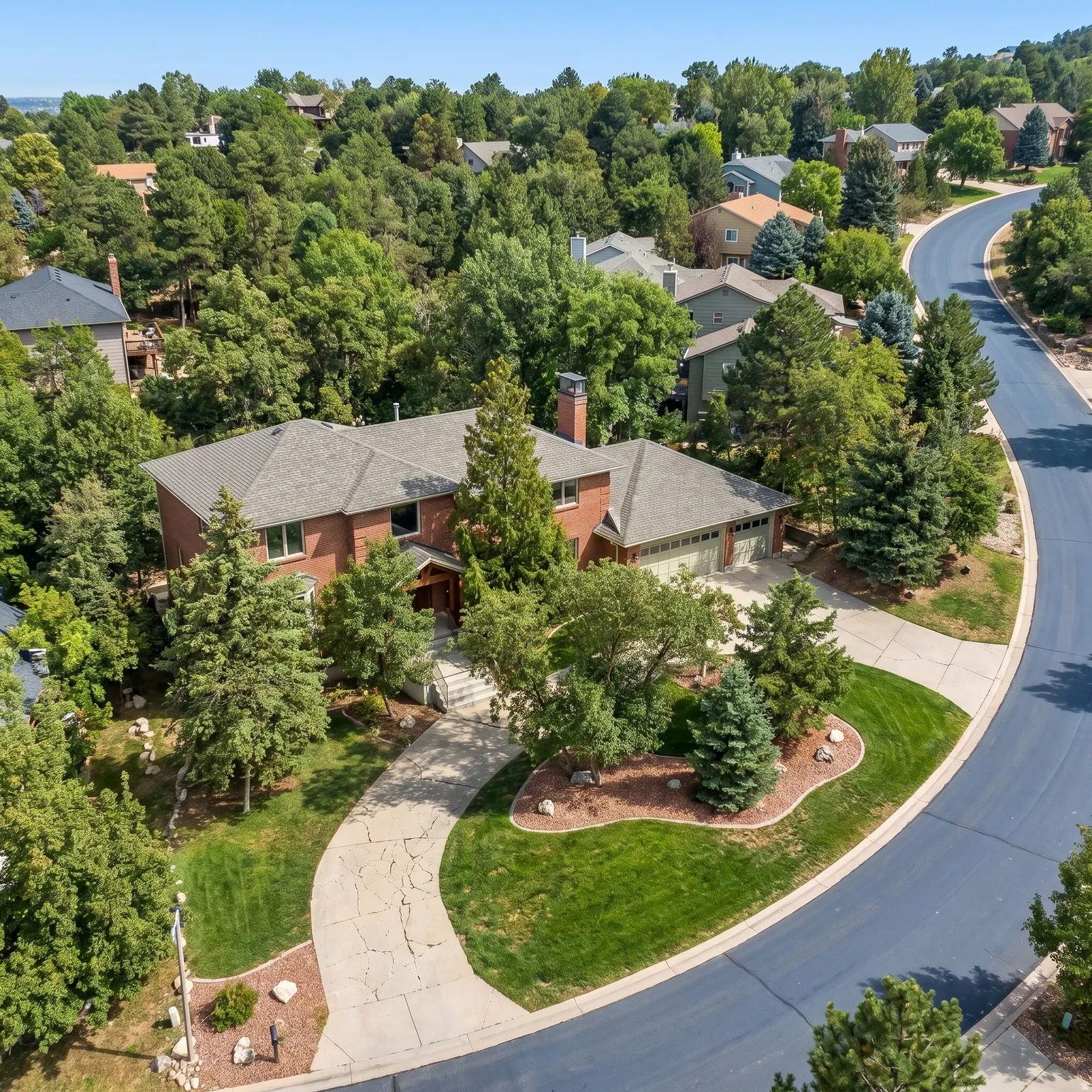 Brick exterior construction with an attached garage, curved driveway, and mature landscaping