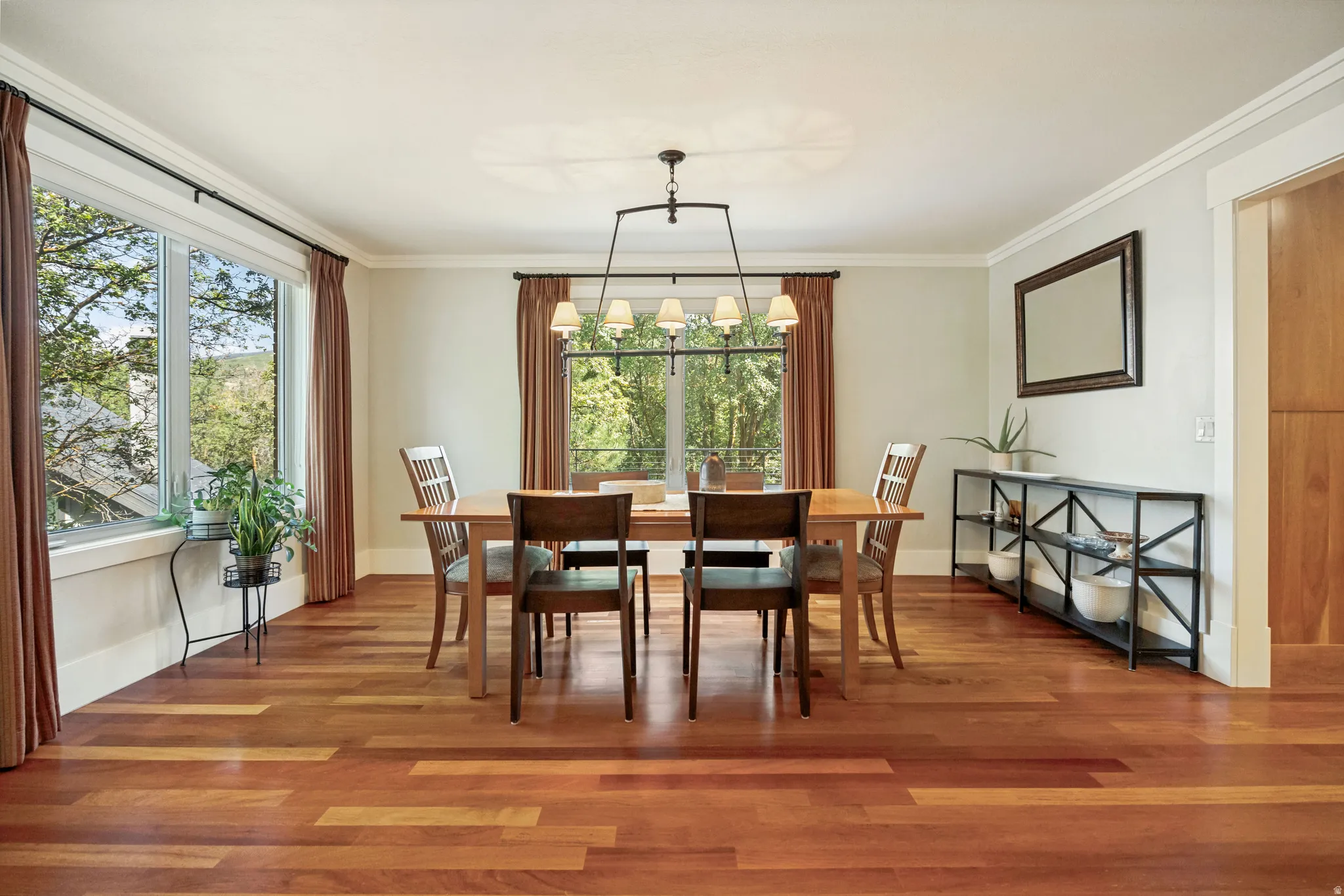 Elegant dining room showcasing rich wood-finish flooring, a large dining table with seating for six, and abundant natural light from multi-pane windows framed with warm drapery