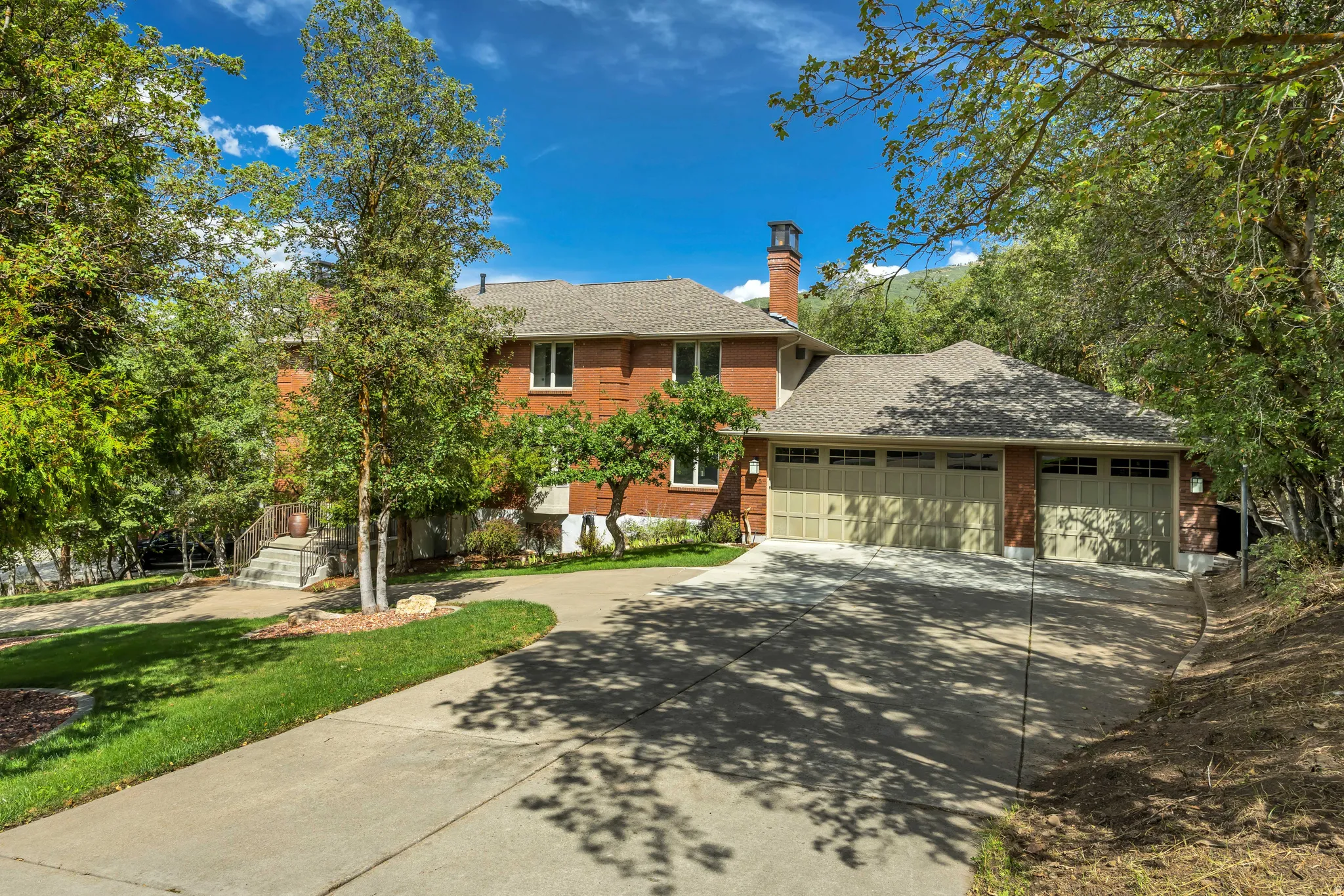Brick exterior, multi-car garage, concrete driveway, mature trees