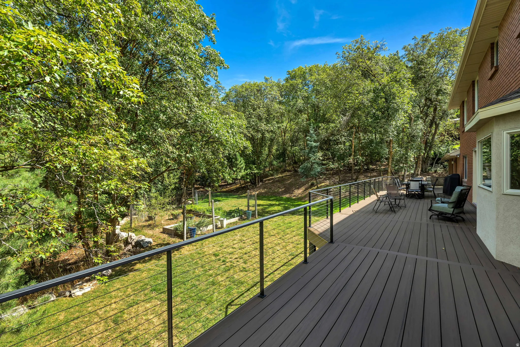 New expansive composite deck with black metal cable railing, overlooking a green lawn with mature trees and landscaped beds