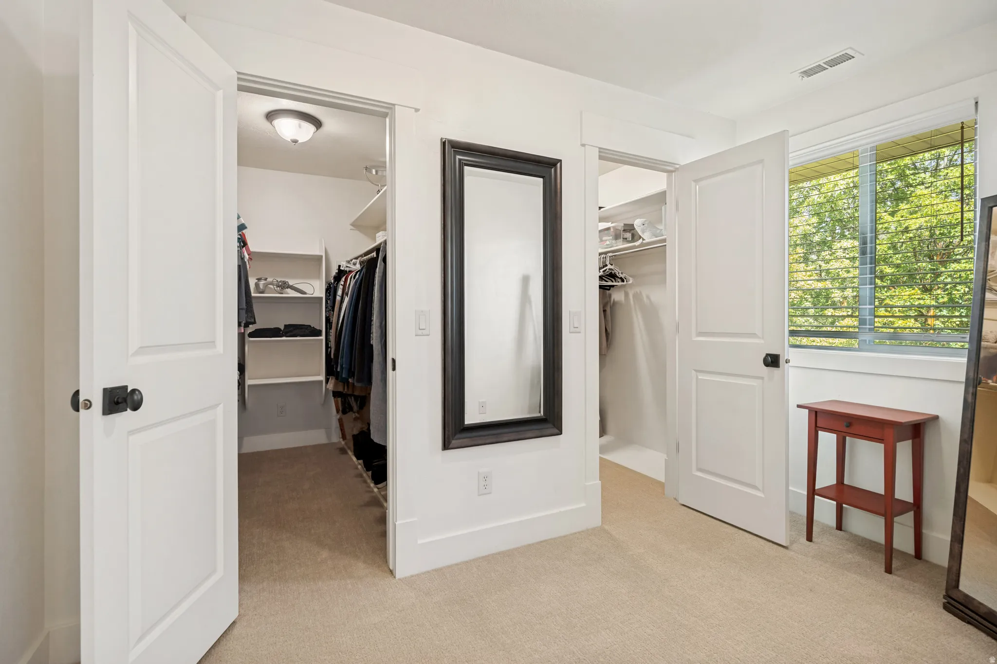 Two walk-in closets with built-in shelving, white trim, and a window with blinds