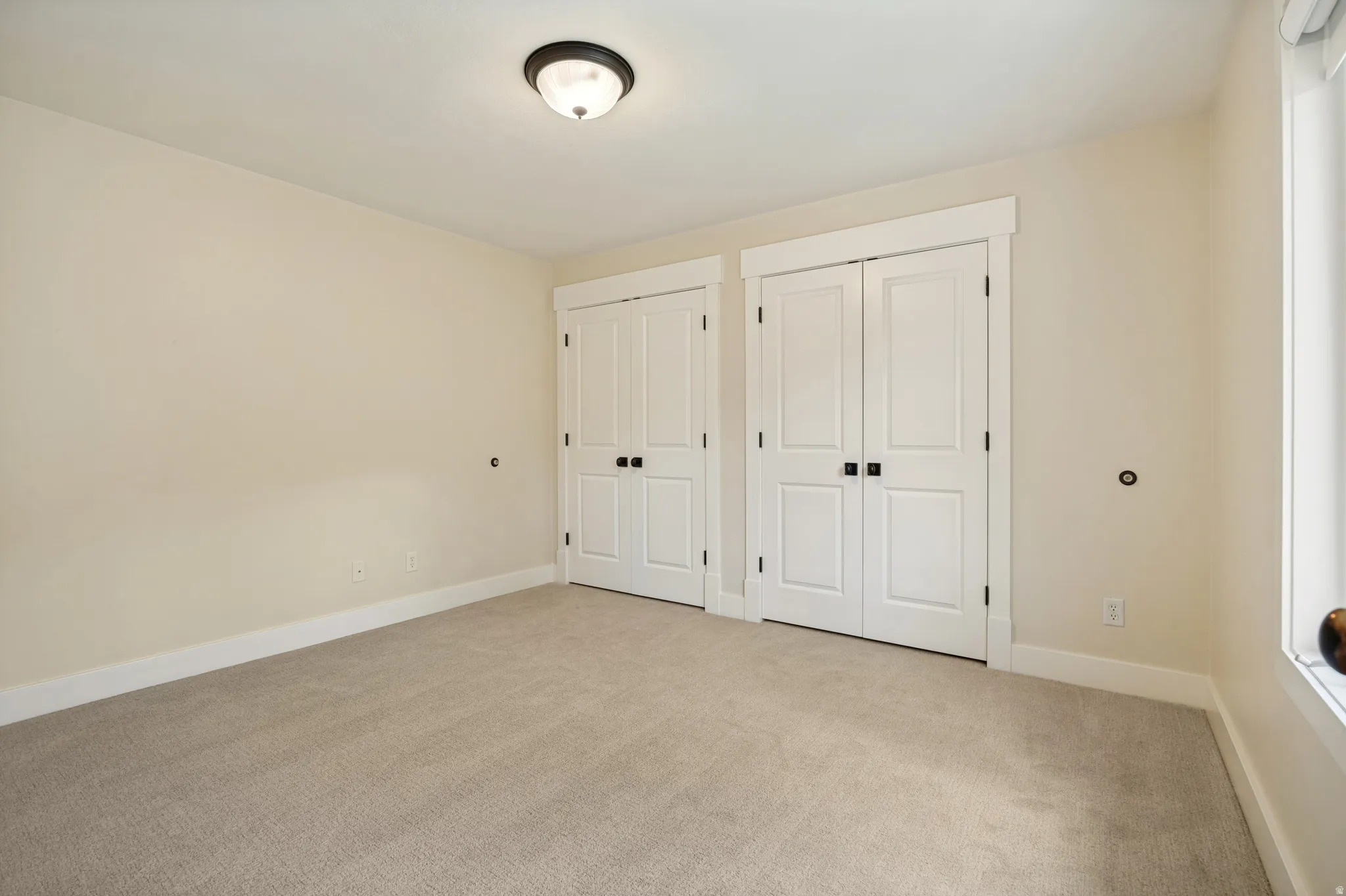 Spacious bedroom featuring neutral carpeting, dual closets with white six-panel doors and black hardware, recessed ceiling lighting, and fresh painted walls throughout