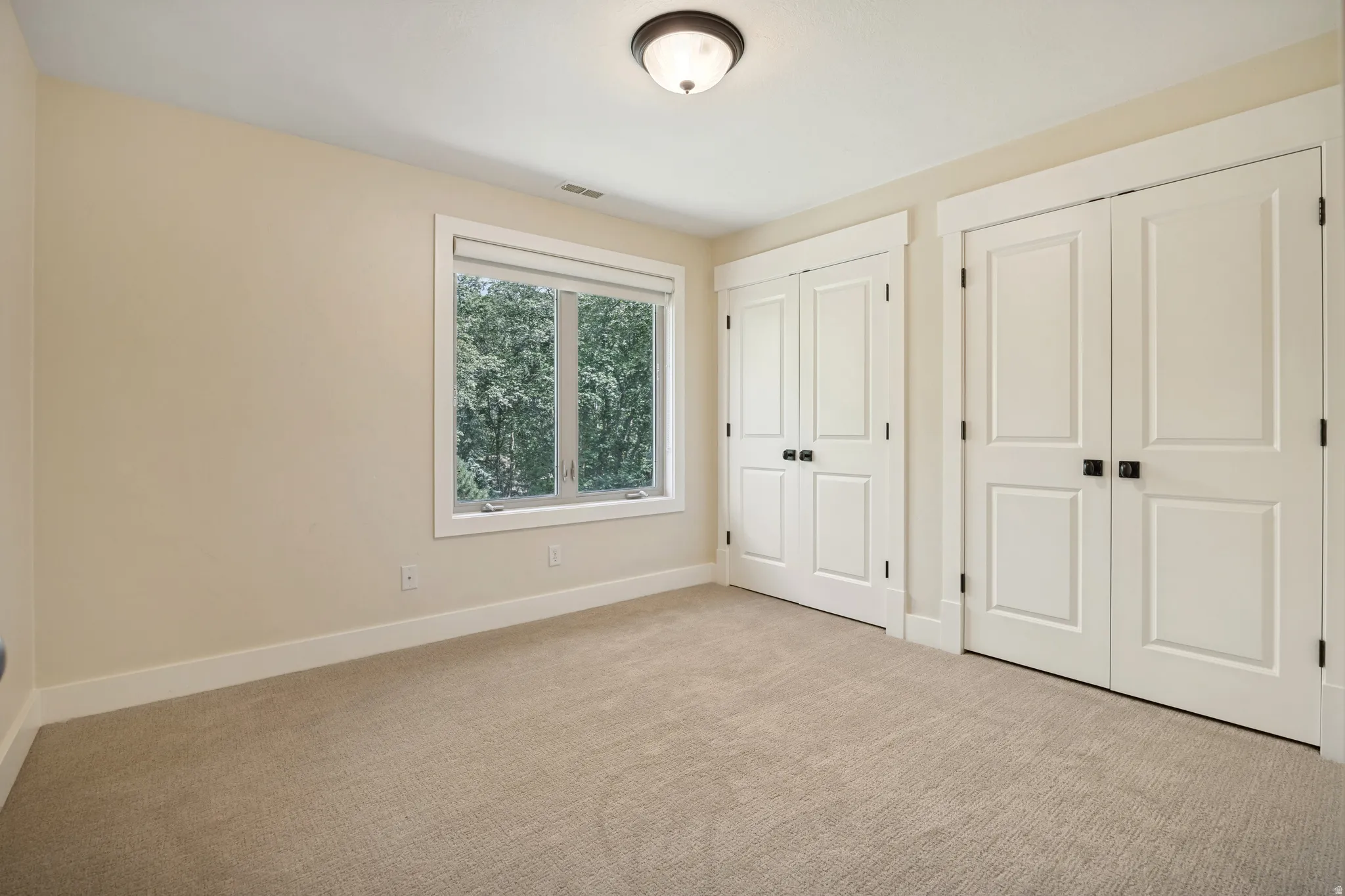 Carpeted room featuring dual bi-fold doors, a single window, and a flush-mount ceiling light fixture