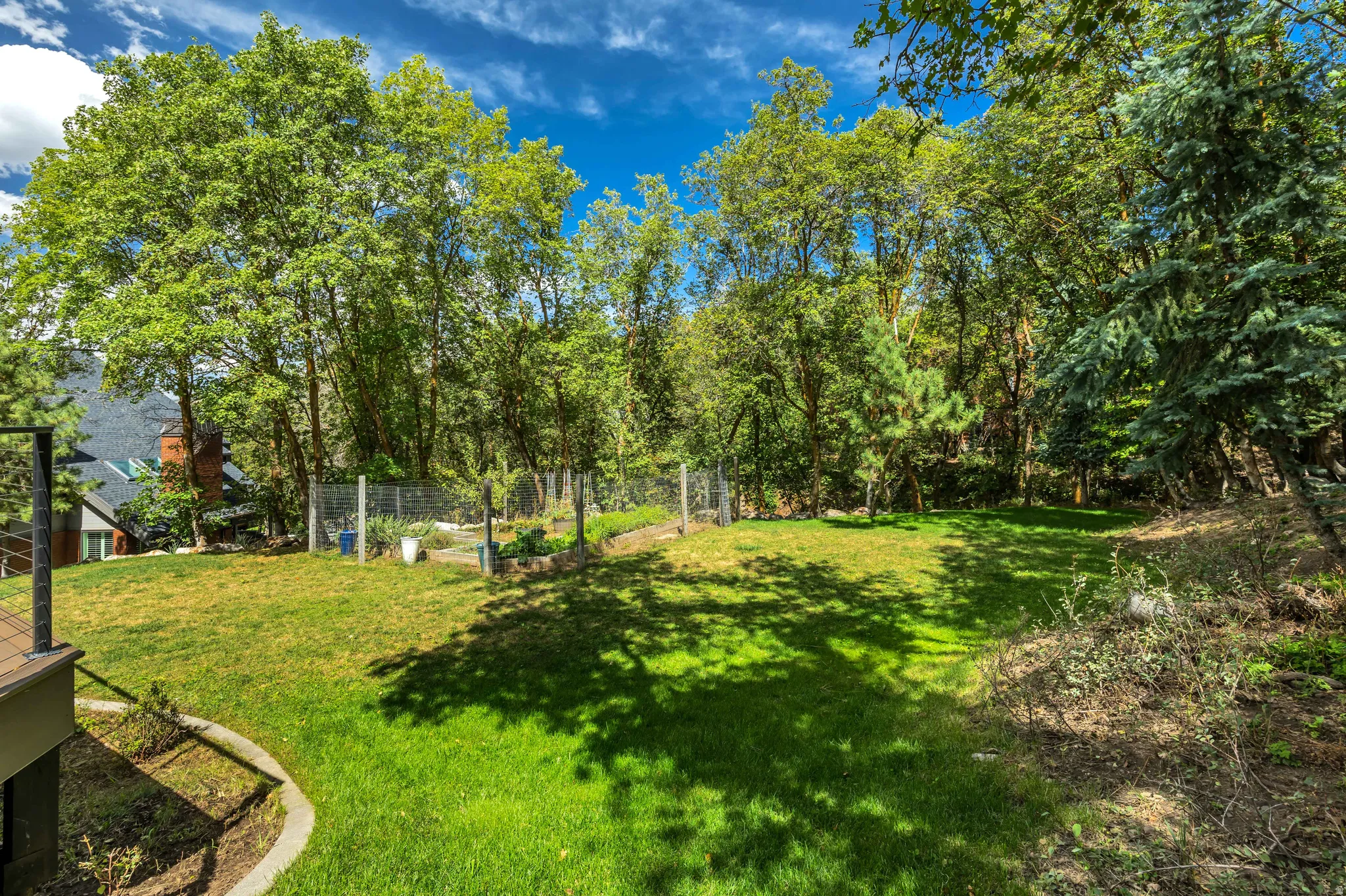 Expansive lawn area surrounded by mature trees, featuring a tiered landscape and a fenced garden plot