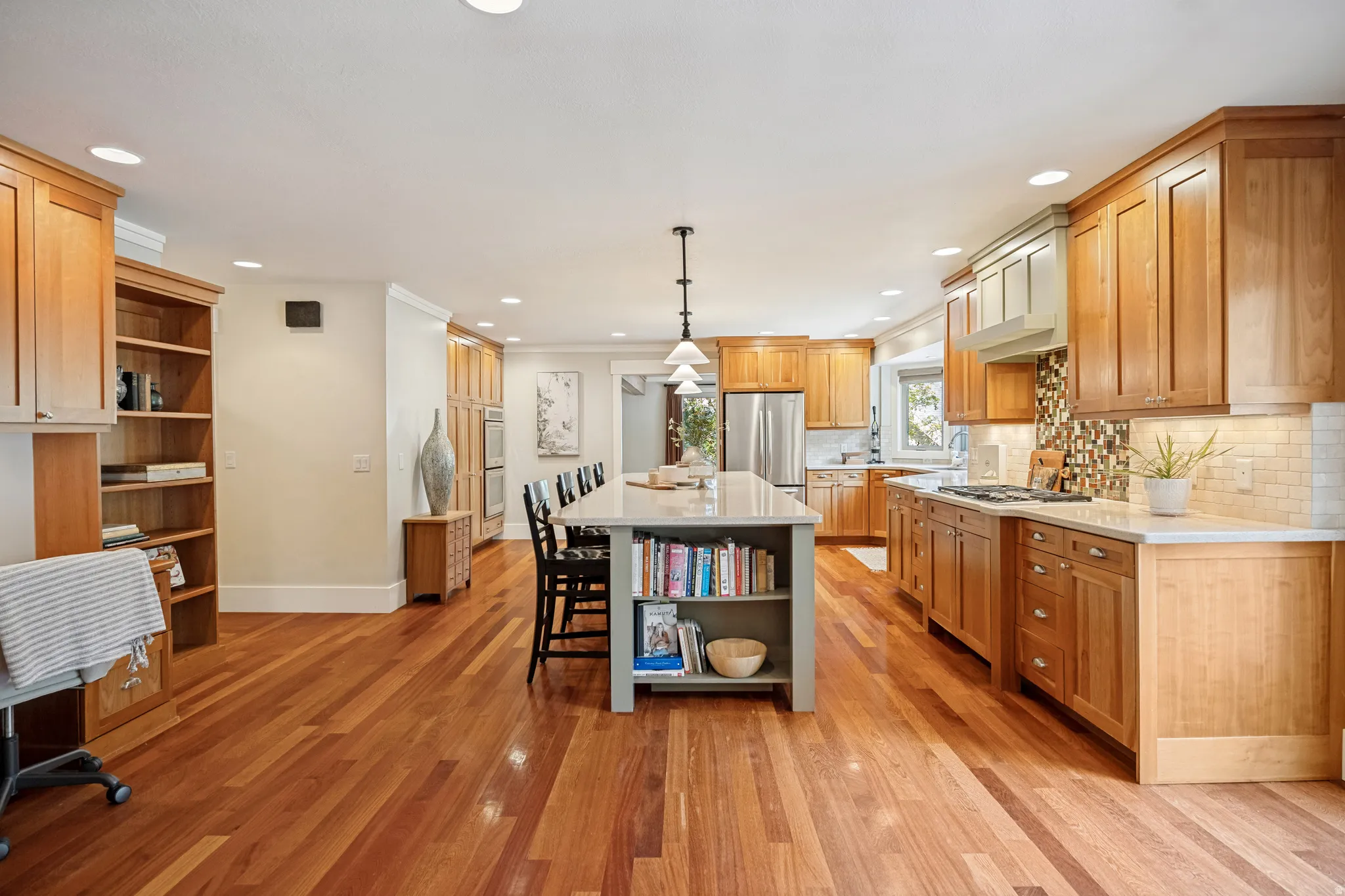 Hardwood flooring throughout, extensive wood cabinetry, double wall ovens, a large kitchen island with built-in shelving, and recessed lighting