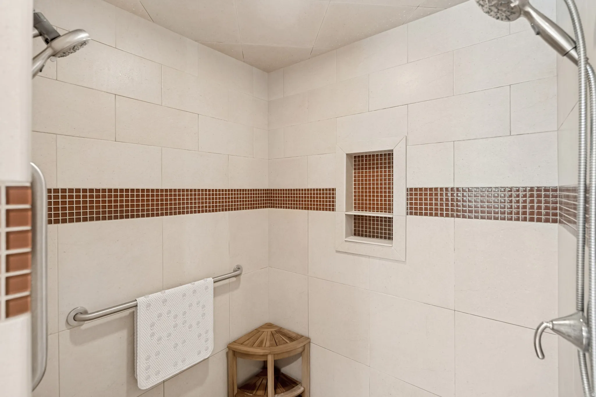Tiled shower surround with decorative mosaic accent, built-in storage niche, and dual shower heads