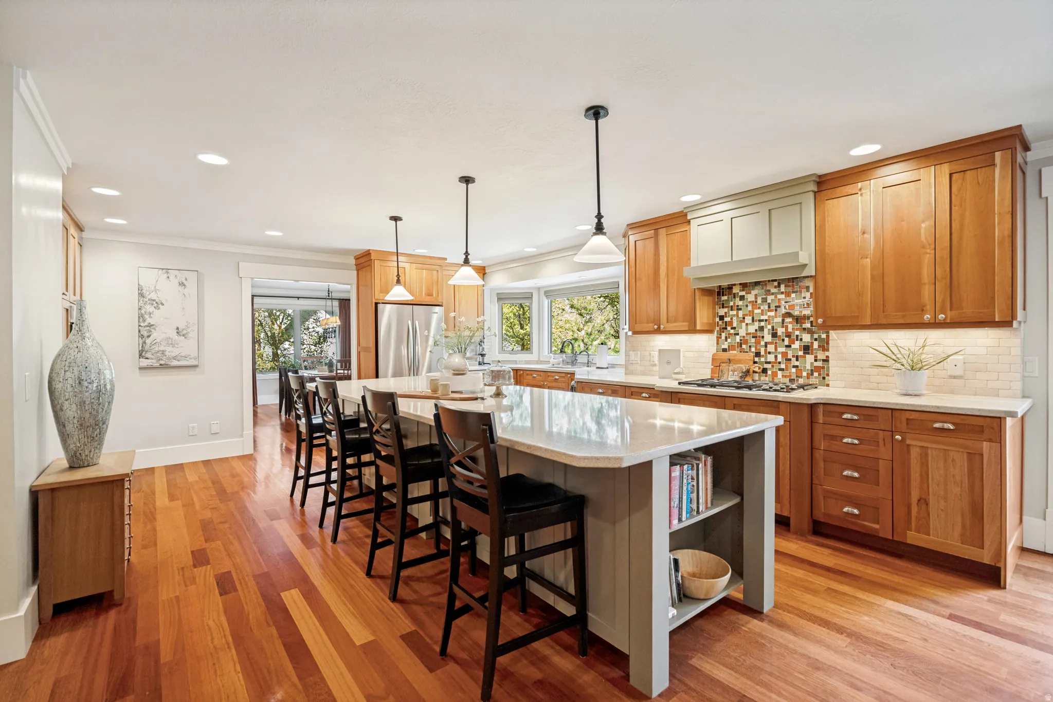 Chef's kitchen featuring warm wood cabinetry, a large center island with quartz countertop and seating for multiple guests, stainless steel appliances, mosaic tile backsplash, and pendant lighting