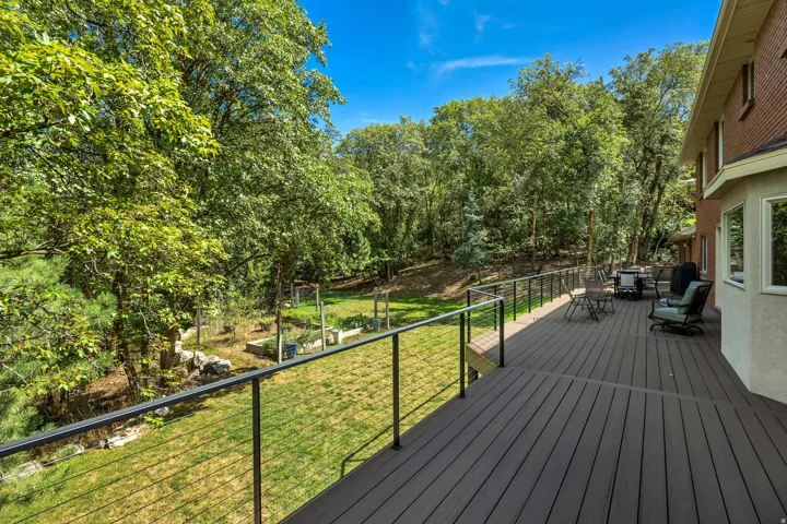 New expansive composite deck with black metal cable railing, overlooking a green lawn with mature trees and landscaped beds