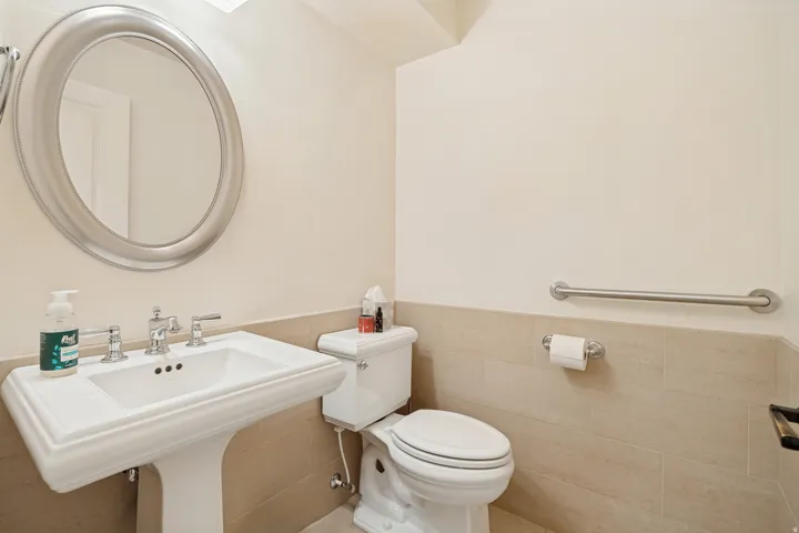 Pedestal sink with chrome faucet, oval framed mirror, wall-mounted grab bar, and tiled wainscoting
