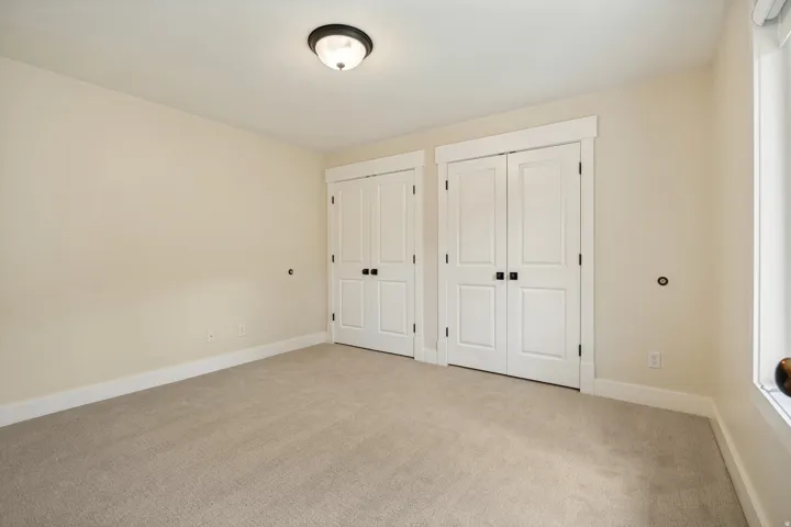 Spacious bedroom featuring neutral carpeting, dual closets with white six-panel doors and black hardware, recessed ceiling lighting, and fresh painted walls throughout