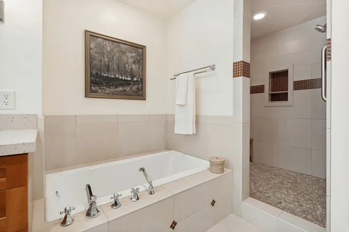 Built-in bathtub, walk-in shower with mosaic tile accents, and a stone pebble shower floor