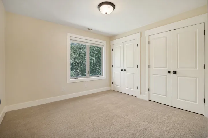 Carpeted room featuring dual bi-fold doors, a single window, and a flush-mount ceiling light fixture