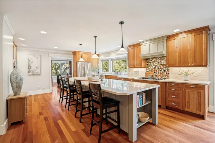Chef's kitchen featuring warm wood cabinetry, a large center island with quartz countertop and seating for multiple guests, stainless steel appliances, mosaic tile backsplash, and pendant lighting