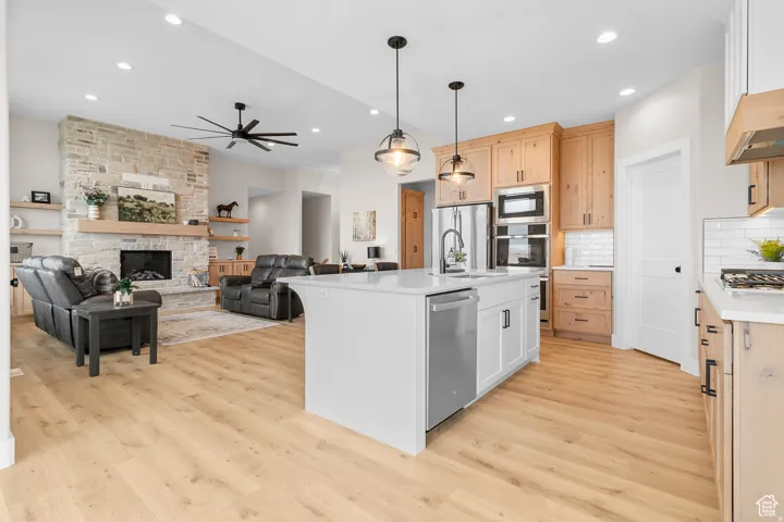 Open-concept living area with wood-finish flooring, a stone-clad fireplace, and a kitchen island with pendant lighting