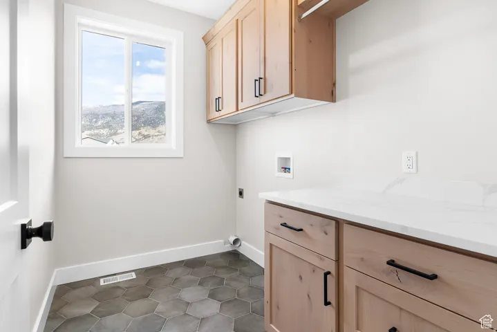 Window with natural scenery, light wood-finish cabinetry, white countertop, hexagon tile flooring, and matte black hardware