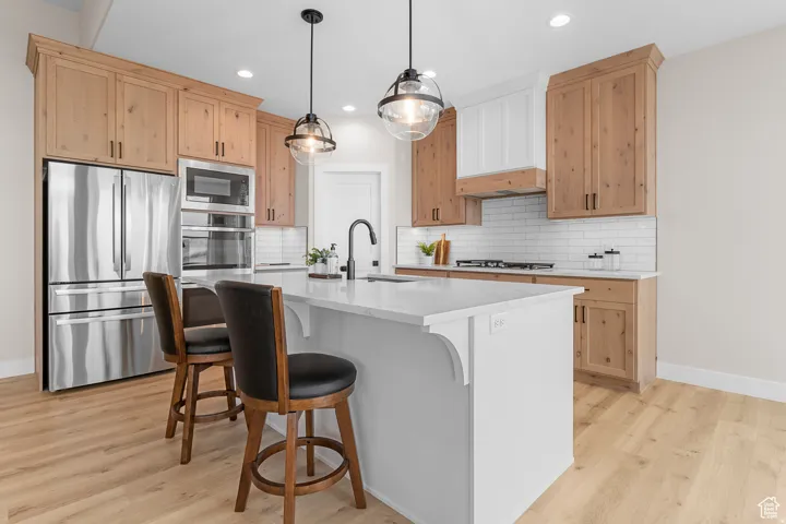Kitchen featuring a central island with a solid surface countertop, stainless steel appliances, wood-finish cabinetry, a subway tile backsplash, and wood-finish flooring