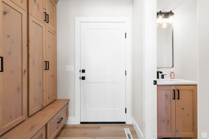 Wood-finish flooring, built-in storage cabinetry, white interior door, vanity with wood-finish cabinetry, and black fixtures