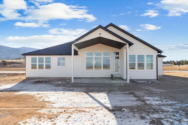 White exterior with black trim, multiple large windows, covered patio, and a mountain backdrop