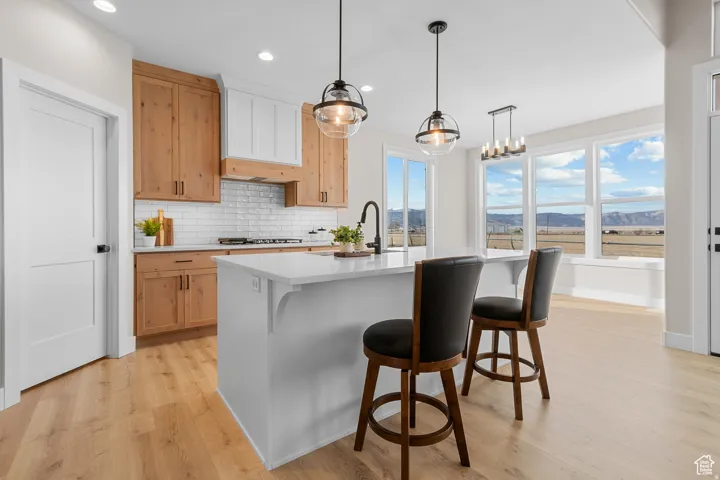 White subway tile backsplash, natural wood cabinetry, central island with white countertop, recessed lighting, and wood-finish flooring