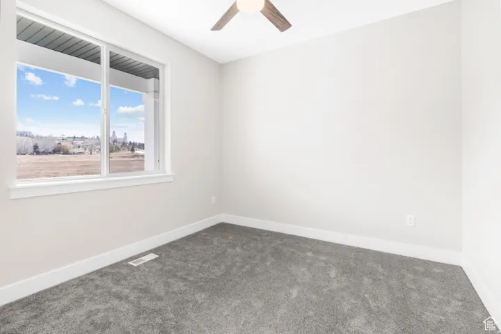Light gray carpeted flooring, white walls, large window, and a ceiling fan with wood-finish blades