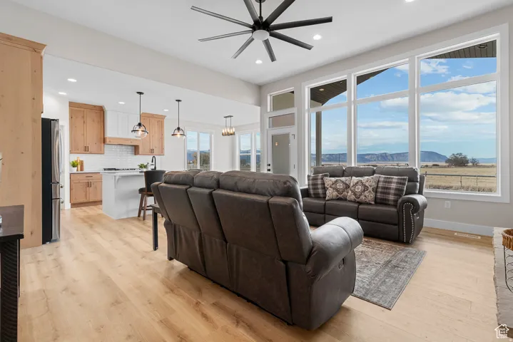 Open-concept living area with large windows, wood-finish flooring, a contemporary ceiling fan, and a kitchen featuring a central island and pendant lighting