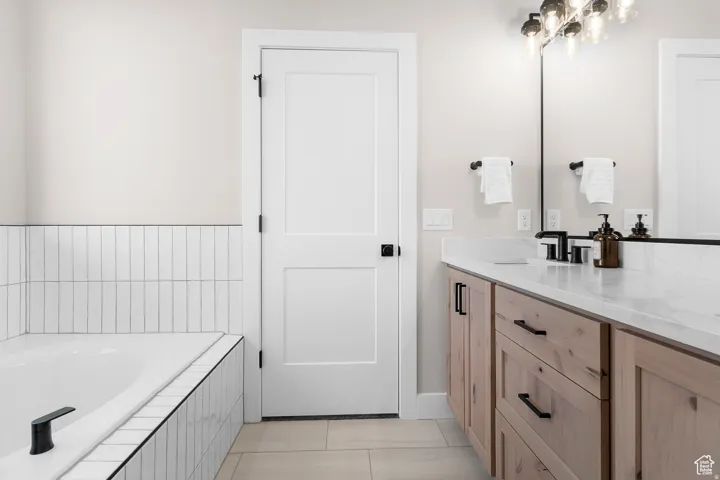 Bathtub with subway tile surround, wood-finish vanity with stone countertop, and matte black fixtures