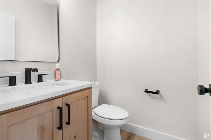 Contemporary vanity with a flat-panel wood cabinet, matte black hardware, white countertop with an integrated sink, and a rectangular black-framed mirror