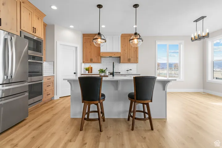 Kitchen featuring stainless steel appliances, wood-finish flooring, a central island with counter seating, and two pendant lights