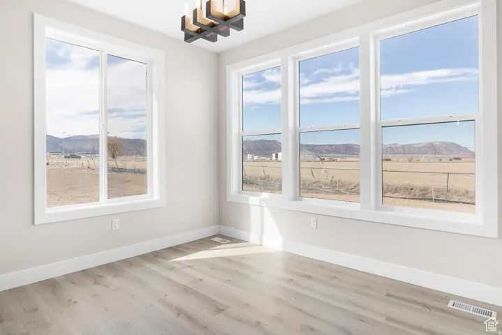 Spacious room with light wood-finish flooring, white trim, and a modern chandelier