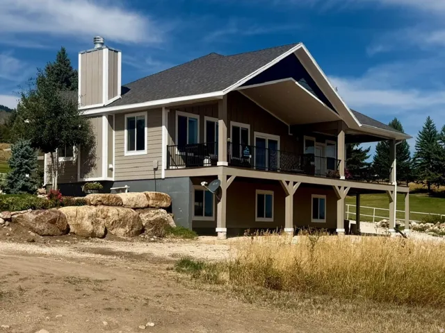 Two-story residence featuring a covered upper-level balcony, a lower-level covered patio, and a stone retaining wall