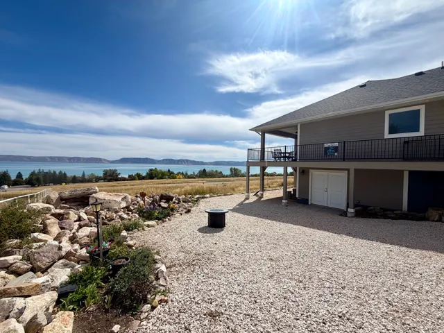 Multi-level exterior with a covered upper-level balcony, ground-level garage access, and a gravel-paved patio