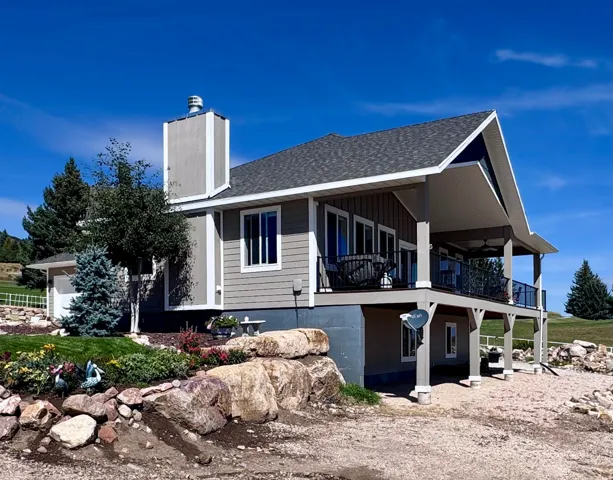 Multi-level residence featuring a covered balcony with a black metal railing, a stone-faced retaining wall, and a side-entry garage