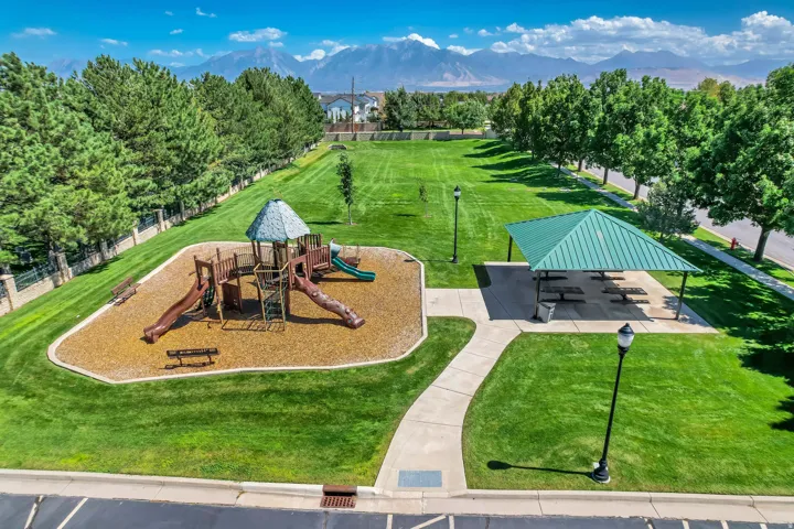 Expansive green space featuring a playground, shaded picnic area, mature trees, and mountain scenery