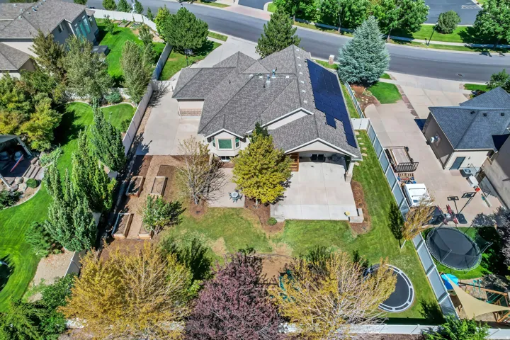 Gable roofline residence with a concrete driveway, attached garage, and a spacious backyard featuring a concrete patio, landscaped garden beds, and mature trees