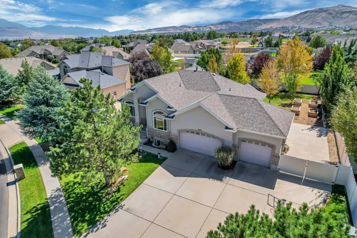 Expansive concrete driveway, attached two-car garage, manicured front lawn, mature trees, and raised garden beds