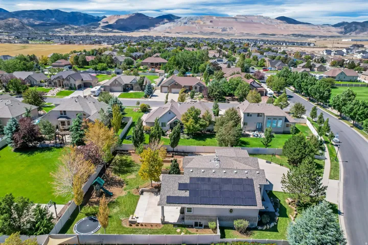 Aerial perspective of a neighborhood featuring houses with landscaped yards, a paved street, and distant mountains